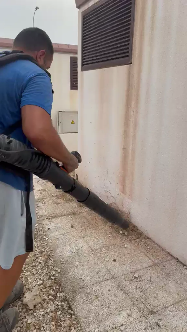 SplendidaClean operative clearing debris from an outdoor communal walkway with a backpack blower